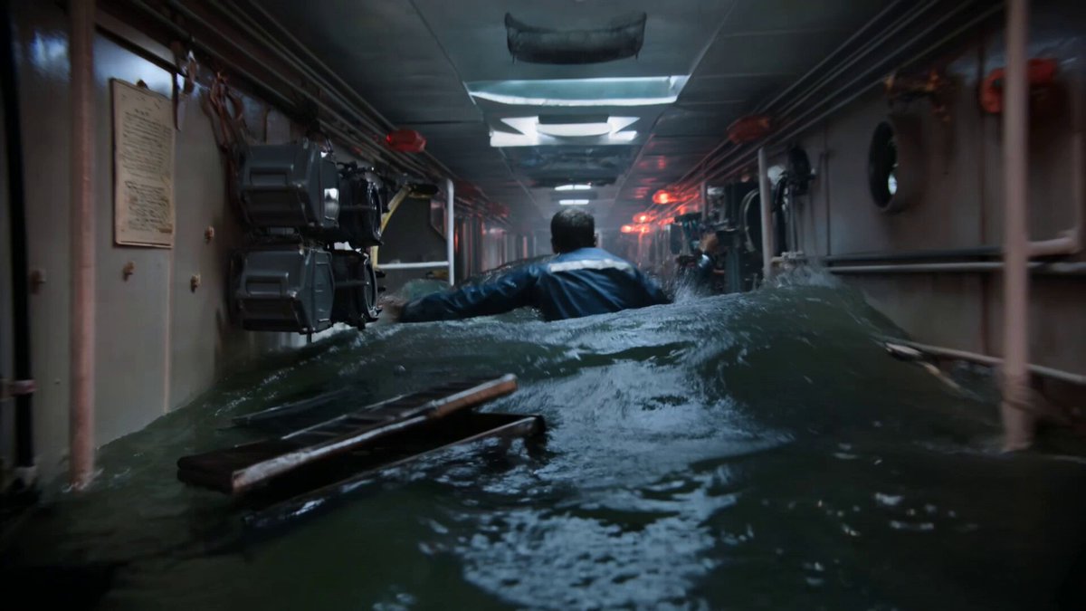 The camera plunges forward through a flooding submarine corr